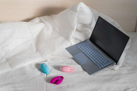 Close-up of several multi-colored clitoral vibrators and a laptop on a white sheet on the bedの写真素材