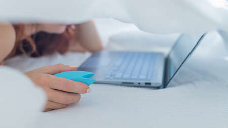 A woman lies in bed holding a clitoral vibrator and watching porn on a laptop. The girl has sex...