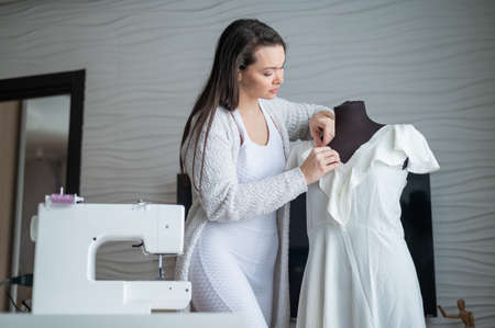 Caucasian woman sews a dress at home. Workspace of a seamstressの写真素材