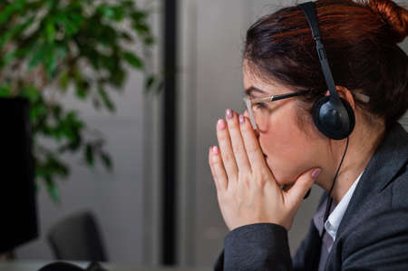 Portrait of woman in headset in frustration holds hands by face in office.の写真素材