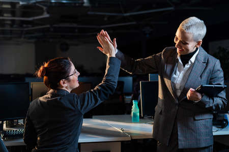 Two young business women are giving five at work. Office workers celebrate successの写真素材