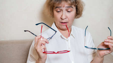 An elderly Caucasian woman chooses glasses from her home collectionの写真素材