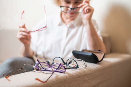 An elderly Caucasian woman chooses glasses from her home collectionの写真素材
