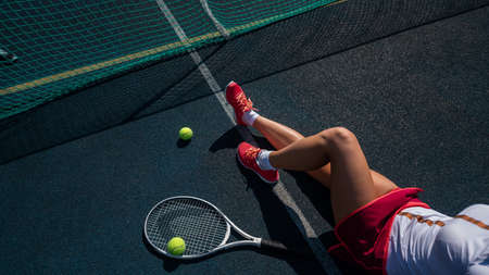A faceless girl in a sports skirt sits on a tennis court and holds a rocket. Top view of female legs.の写真素材