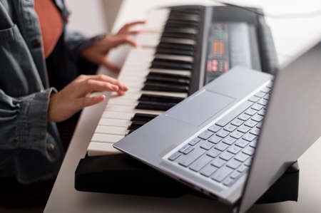 Close-up of female hands on the electric piano. A woman is learning to play the synthesizer on a laptopの写真素材