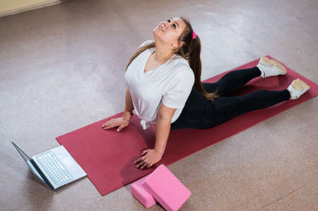 Young Plus Size Woman Stretching At Home Online. Flexible girl practices yoga and watches an online...
