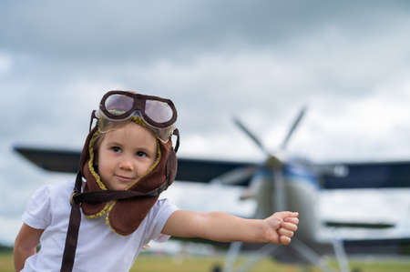 A cute little girl dressed in a cap and glasses of a pilot on the background of an airplane. The...