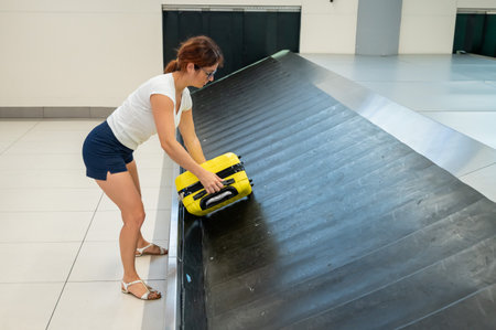 Caucasian woman picks up her yellow suitcase from the luggage belt at the airport terminal.の写真素材