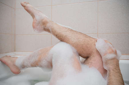 Funny picture of a man taking a relaxing bath. Close-up of male feet in a bubble bath. Top viewの写真素材