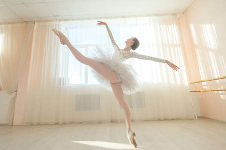 Beautiful ballerina in body and white tutu is training in a dance class. Young flexible dancer posing in pointe shoes.の写真素材