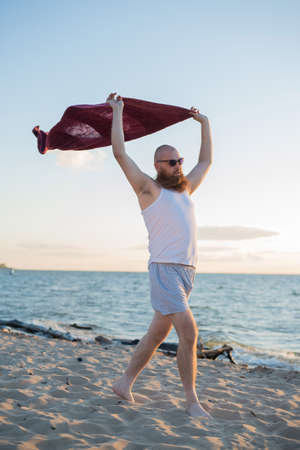 Brutal man posing on the beach. A parody of a glamorous girl.の写真素材