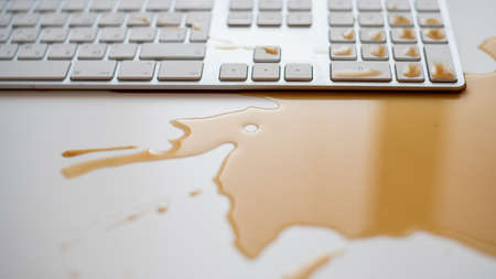 Spilled drops of black coffee on a white computer keyboard