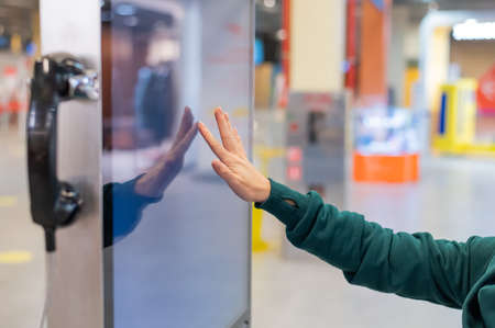 Faceless woman in medical mask uses electronic information board in a public placeの写真素材