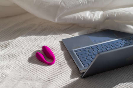 Clitoral vibrator and laptop on the bed in a white sheetの写真素材