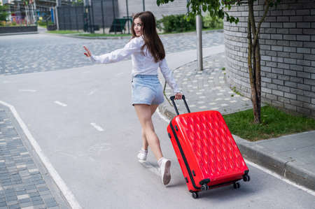 Happy beautiful caucasian woman is running with a big red suitcase outdoors. Excited girl is late for the plane.の写真素材