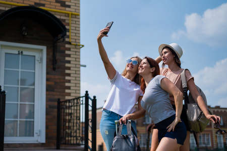 Three happy girls friends go on a trip and take a selfie on a mobile phone. The blonde brunette and...