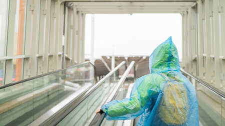A woman in a raincoat rises on an escalator. Girl in protective clothing from the rain. Back view.の写真素材