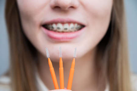 Close-up portrait of a woman with braces on her teeth holding a brush.の写真素材