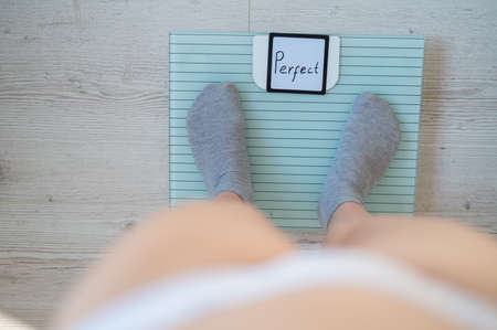 Faceless woman measures weight on the floor scales. Top view of womens feet in gray socks on the scales with the word perfect. The inscription on the screen is perfect. There is no excess fat.の写真素材