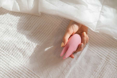 A faceless woman lies in bed under a blanket holding a clitoral vibrator.の写真素材