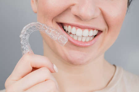 Close-up portrait of a woman holding a plastic transparent retainer. A girl corrects a bite with the...