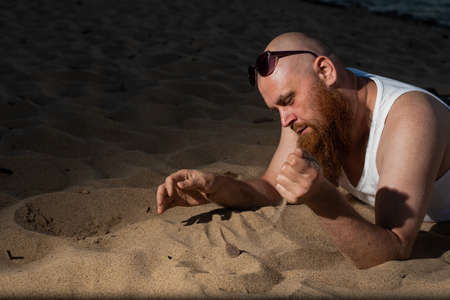 A humorous portrait of a brutal man in a T-shirt and boxers on the beach at sunsetの写真素材