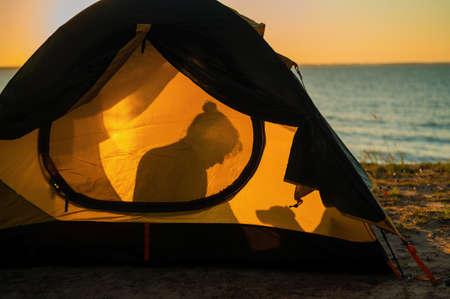 Woman and dog in a tourist tent at sunset. Camping with a petの写真素材
