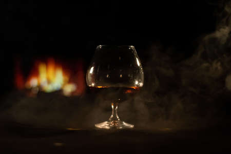 A glass of brandy and cigar smoke in the dark on the background of the fireplace. Gentlemens club conceptの写真素材