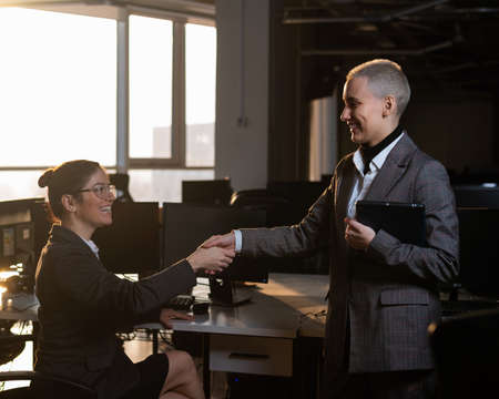 Two young business women shake hands at work. The office staff made a dealの写真素材
