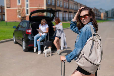 Three girlfriends travel by car with a dog and load suitcases into the trunk.の写真素材