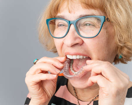 A happy elderly woman puts on transparent removable braces. Cosmetic dentistry for all ages
