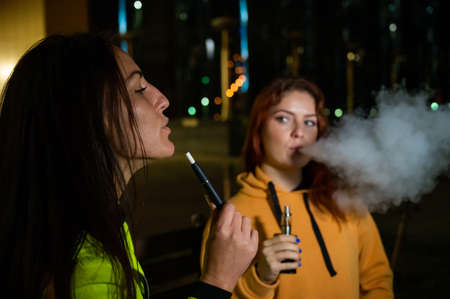 Two caucasian women smoke vape and hookah outdoors at night.の写真素材
