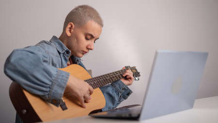 Young woman is learning to play the guitar online. Remote music lessons on a laptopの写真素材