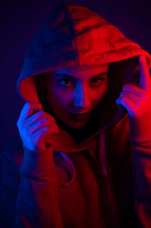 Portrait of a beautiful young woman in a sweatshirt with a hood in neon lightの写真素材