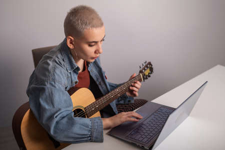Young woman is learning to play the guitar online. Remote music lessons on a laptopの写真素材