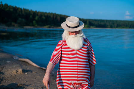 An elderly man in a classic bathing suit walks along the beach with an umbrella on a hot summer dayの写真素材