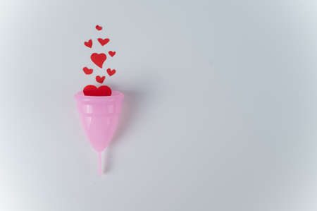 Pink menstrual cup and hearts imitating blood on a white background. Reusable personal hygiene...
