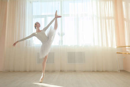 Beautiful ballerina in body and white tutu is training in a dance class. Young flexible dancer posing in pointe shoes.の写真素材