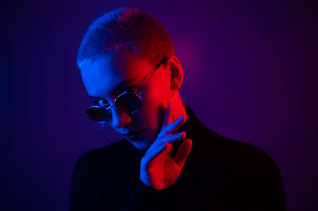Portrait of a beautiful young woman with short hair in sunglasses in neon lightの写真素材