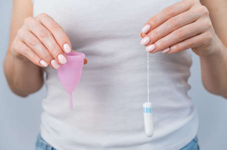 Close-up of a woman holding a pink menstrual cup and tampon against a white backgroundの写真素材