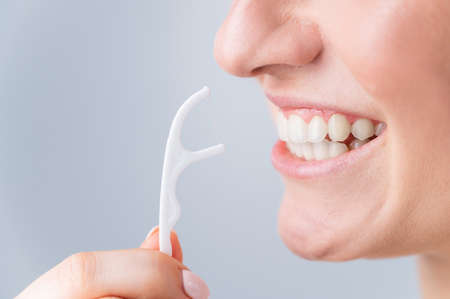 Caucasian woman brushing teeth with toothpick with dental floss on white background.