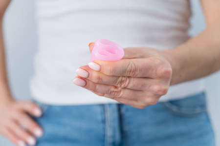 A faceless woman holds a folded pink menstrual cup. Alternative to tompons and padsの写真素材