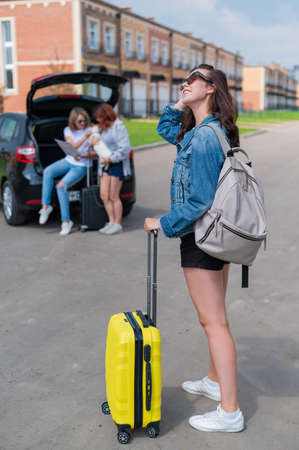 Three girlfriends travel by car with a dog and load suitcases into the trunk.の写真素材