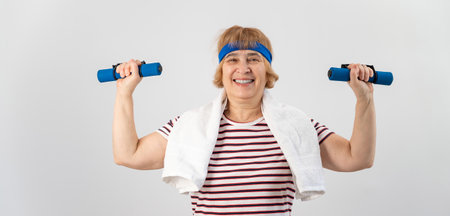 An elderly woman with a blue bandage on her head trains with dumbbells on a white background