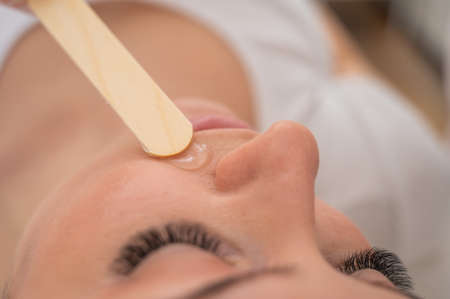 The master applies the anesthetic gel with a spatula to the womans face before laser depilation. Mustache removalの写真素材