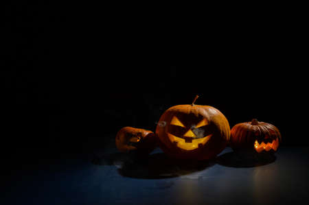 Pumpkins with carved grimaces and candles inside in the dark for halloween. Jack o latern in smoke.の写真素材