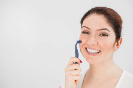 Caucasian smiling woman shaves face with razor on white background. Empty space.の写真素材