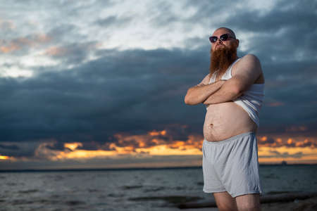 Humorous portrait of a brutal man posing on the beach at sunsetの写真素材