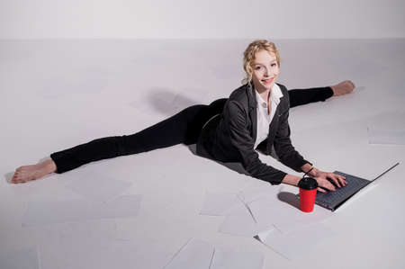 A ballerina dressed in a business suit sits in a middle twine, works at a laptop and drinks coffee....
