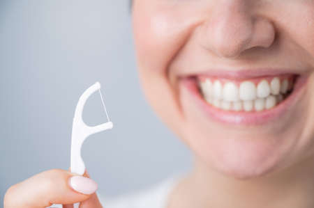 Close-up portrait of a beautiful caucasian woman with a flawless smile holding a toothpick with dental floss on a white backgroundの写真素材